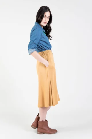 A mustard knit midi skirt seen from the side, flaring below the pocket.