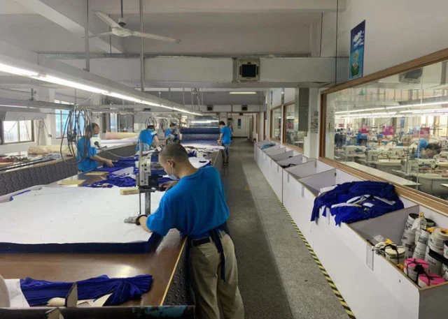 Workers at long cutting tables in a sportswear factory.