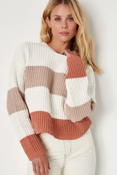 A woman in a striped crewneck sweater in cream, tan and rust.