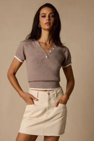 A woman in a taupe short-sleeve ribbed knit polo with contrast tipping.