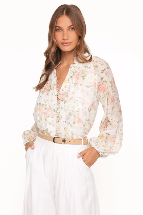 A white floral blouse with a lined bodice and sheer gathered sleeves, tucked into white trousers.
