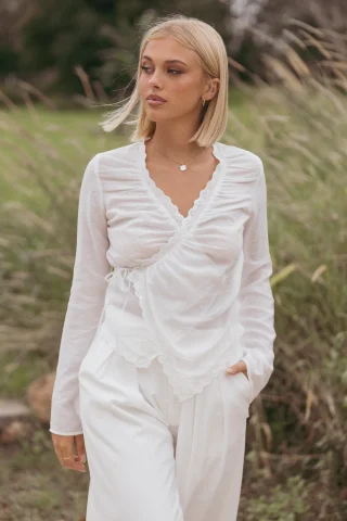 A white wrap blouse with a lace-edged V-neck and a tie at the side of the waist.