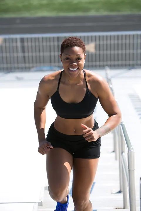 A woman in a black sports bra and running shorts runs up stadium steps.