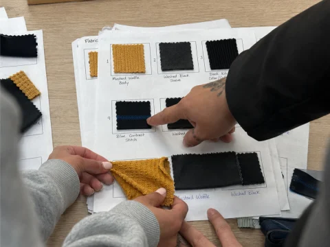 Mustard and black fabric swatches with ribbing laid on spec sheets during the trim review.