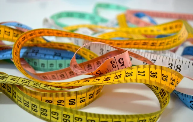 A tangle of yellow, orange, blue and green tape measures on a white table.