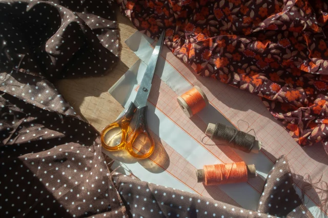 Dressmaking scissors and spools of thread on pattern paper between a polka-dot fabric and a floral print.