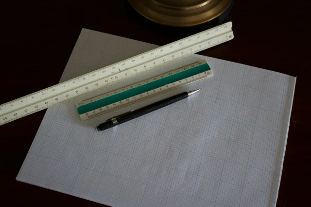 A ruler, a pen and a sheet of pattern paper on a dark work table.