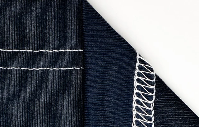 A navy knit hem with two rows of white coverstitch, folded back to show the looper threads on the underside.