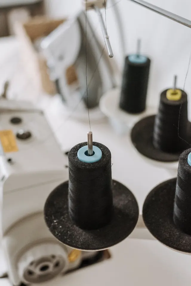 Cones of black thread feeding an overlocker in a bright workroom.