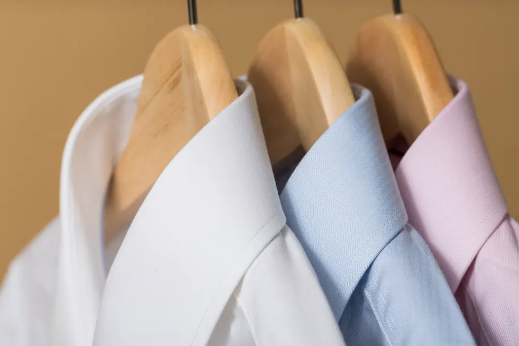 Collars of white and blue dress shirts on wooden hangers.