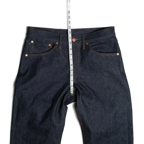 A tape measure laid along the front rise of dark blue jeans, from the crotch seam to the waistband.