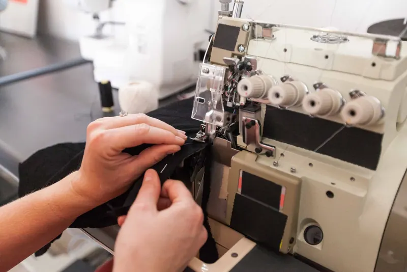 Hands guiding black knit fabric through an overlock machine.