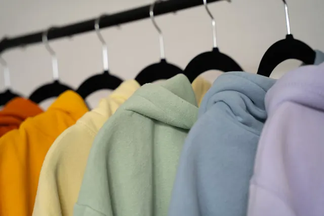 Hoodies in orange, cream, sage, blue and lilac hanging on a rack.