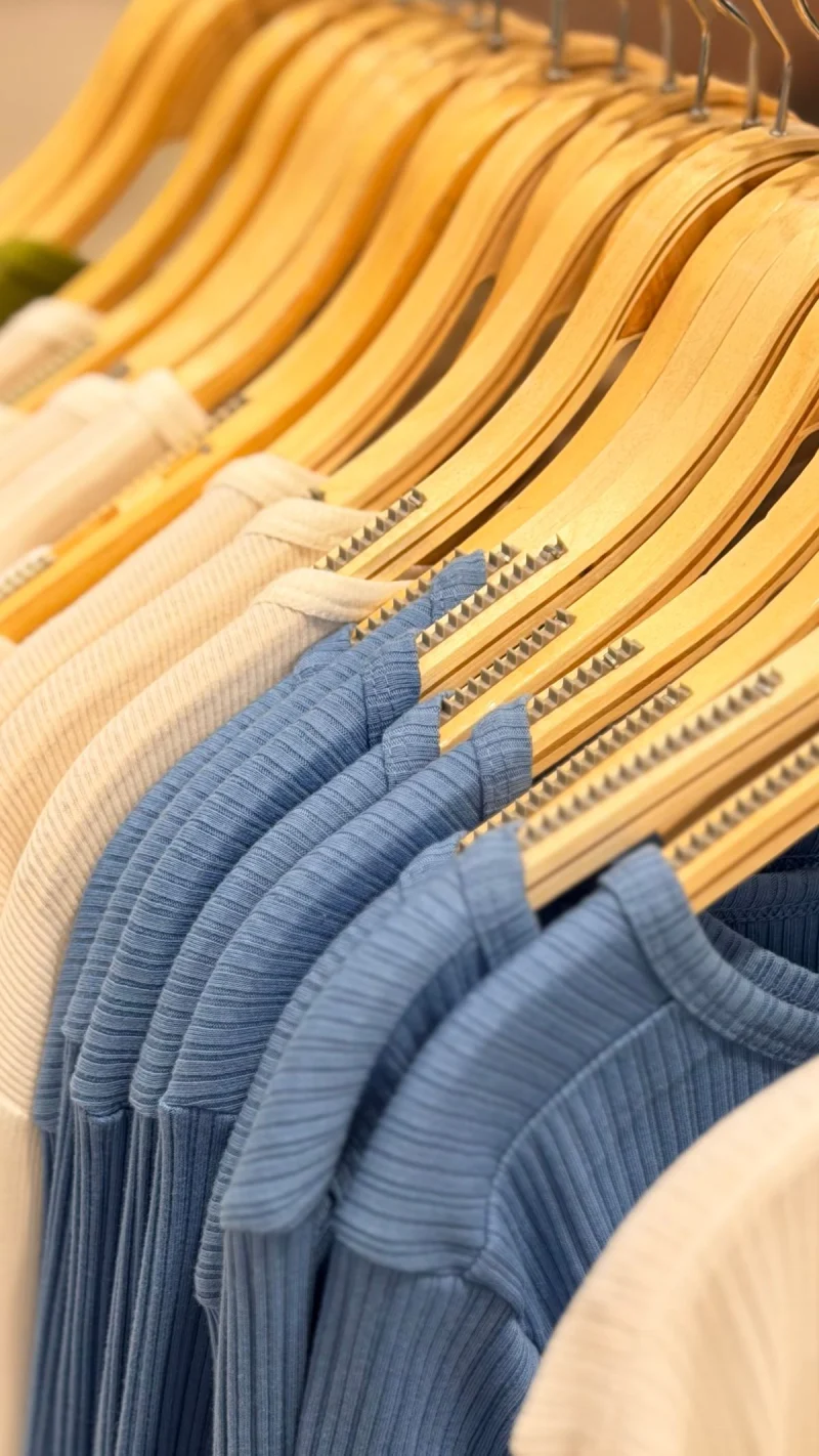 Blue and cream ribbed knits on wooden hangers along a rail.
