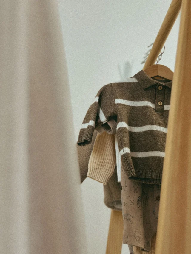 A child's striped polo-collar sweater on a wooden hanger.