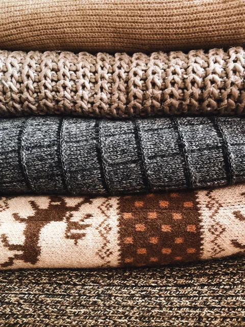 Folded knit sweaters stacked up, one with a jacquard band of reindeer and dots.