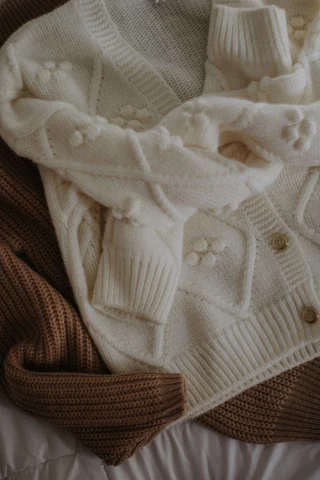 A cream knit cardigan with bobble flowers and wooden buttons lying over a brown knit.