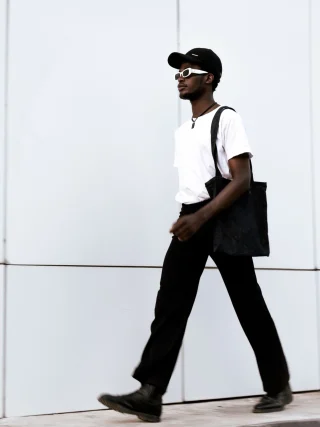 A man walking with a black tote on his shoulder.