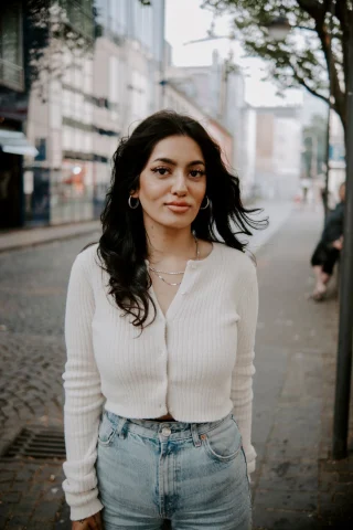 A woman in a cropped white ribbed cardigan buttoned over high-rise jeans.
