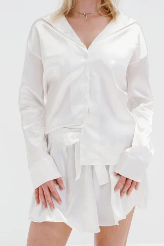 A model in a white satin pajama shirt and shorts against a white background.
