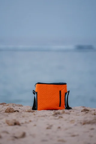 An orange insulated cooler bag on a beach.