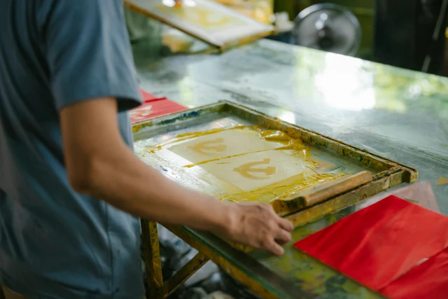 A screen printer pulling yellow ink through a screen.