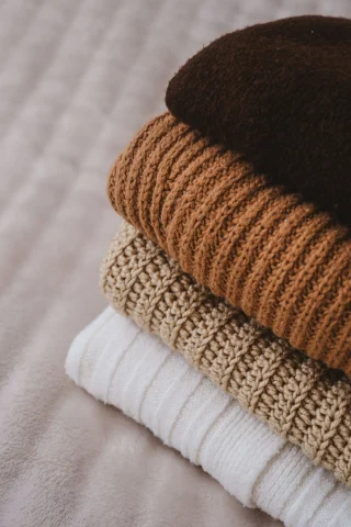 Folded ribbed knits in brown and cream tones piled on a soft throw.