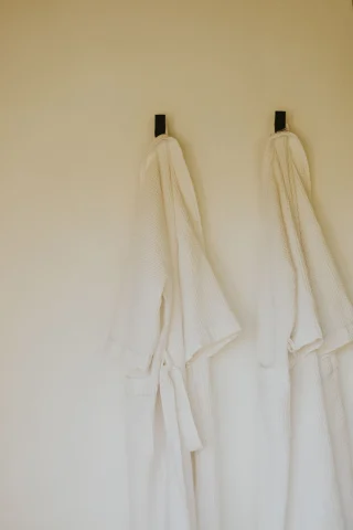 Two white bathrobes hanging on wall hooks.