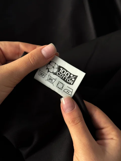 Hands holding a 100% cotton care label with washing symbols.