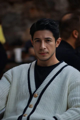 A man in a white button-front cardigan with black trim along the front edges.
