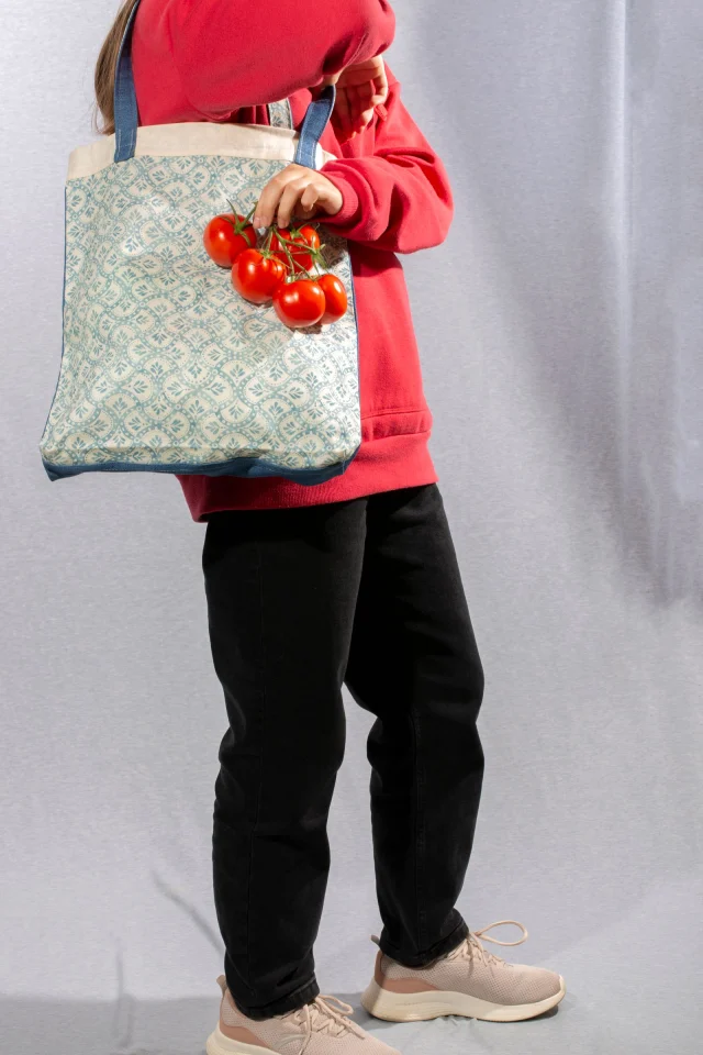 A shopper holding a bunch of tomatoes beside a tote with an all-over blue print.
