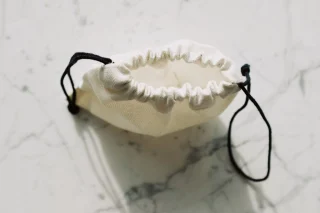 An open cotton drawstring bag with black cords on a marble surface.