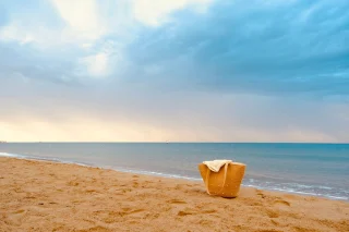 A yellow tote bag left on a sandy beach at sunrise.