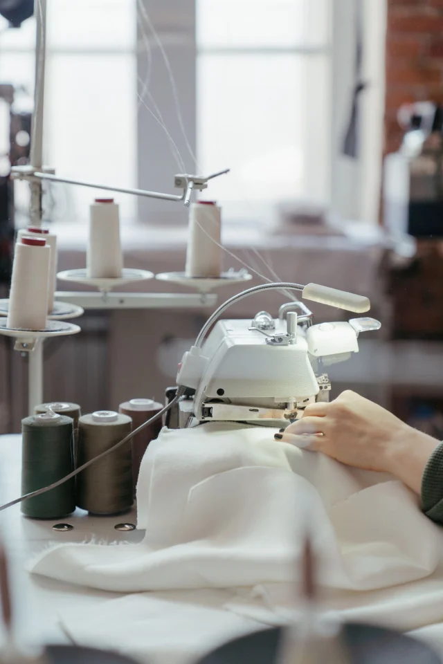 An overlock machine sewing white fabric beside cones of thread.