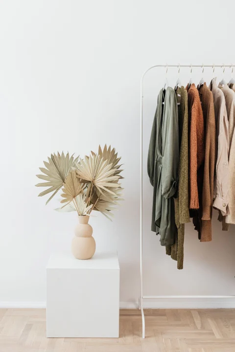 Earth-toned cardigans and knits on a clothing rail in a white room.