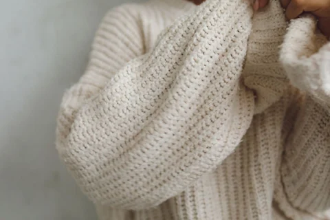Hands pulling the long sleeves of a chunky cream wool cardigan.