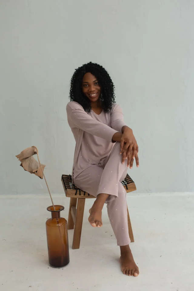 A woman in a mauve lounge set sitting on a wooden stool.