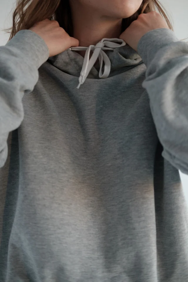 A person in a gray hoodie holding the hood at the neck, with the drawcord hanging from it.