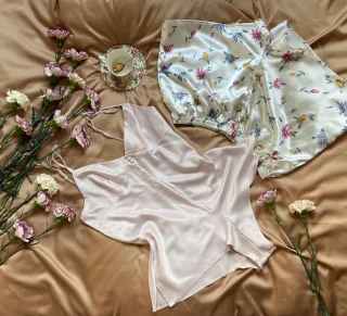 A pale pink satin cami and floral print shorts laid out with fresh flowers.
