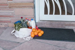 A white reusable tote with groceries and oranges on a doorstep.