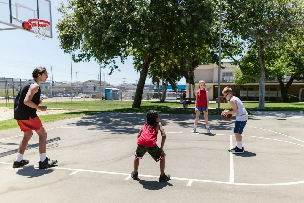 Kids in a pickup game on a sunny outdoor basketball court.