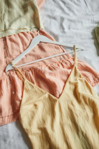 Pastel camisoles and sleep shorts on hangers over a bed.